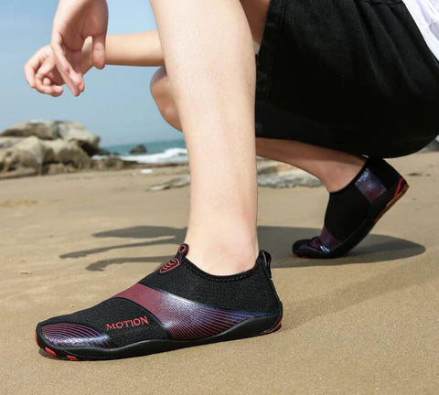 Uomo con scarpe da spiaggia Motion Rouge d'Aquashoes marchant sur le sable