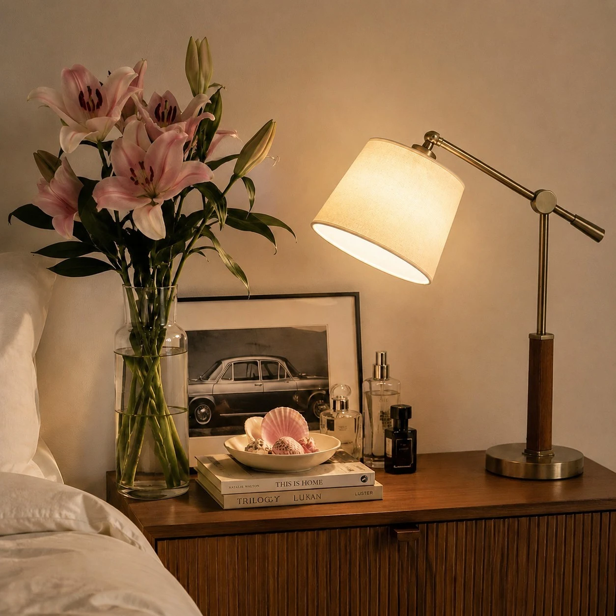 Lámpara de mesa blanca con brazo articulado, encendida junto a libros y flores.